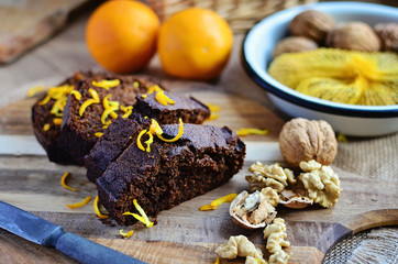 Christmas chocolate cake sliced on the wooden board. Sweet dessert with walnuts and oranges. Close up.