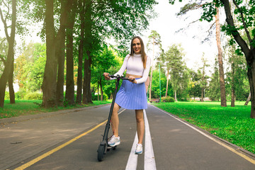 A girl in a white t-shirt and blue skirt riding on a scooter in the Park