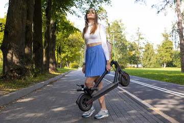 Fototapeta premium Girl carries her folded electric scooter in the park