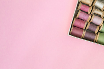 Colorful sewing threads lie in a box in a row gradient on a green background, selective focus. There is a place for text.