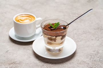 Portion of Classic tiramisu dessert in a glass cup and espresso coffee on concrete background