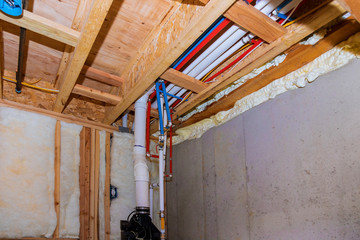 New home under construction plumbing PVC pipes inside a home framing with basement view