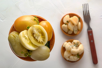 Salted tomatoes in a wooden plate on a background of fermented products on a white table. Close-up. Top view