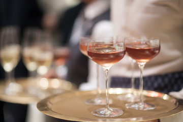 Blurry background of the waiter holds the tray with a glass of champagne to be served to the customer.