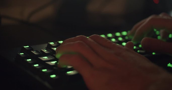 Hands Typing on Gaming Keyboard Glowing Green in Dark Room 