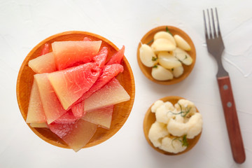 Salted watermelons in a wooden plate on a background of fermented products on a white table. Close-up. Top view