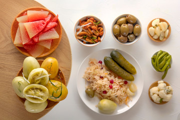 Pickled watermelons and mushrooms in a wooden bowl on a background of fermented products on a white table. Close-up. Top view