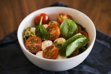 Caprese salad variation with pesto and spinach in white bowl on walnut table