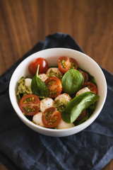 Caprese salad variation with pesto and spinach in white bowl on walnut table
