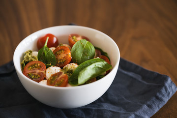 Caprese salad variation with pesto and spinach in white bowl on walnut table