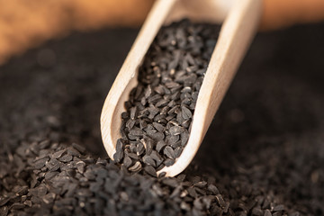 Macro view of dried seeds of black cumin seeds kalinji on wooden spoon. Close up shot with...