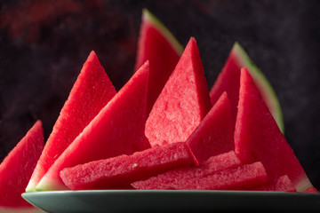 Fresh sweet spanish watermelon sliced on green plate on dark background. Low key close up shot with selective focus