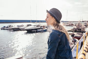 Fototapeta na wymiar Charming girl tourist enjoys the sunshine standing on the pier and admiring the sea landscape. The concept of vacation at sea in the summer