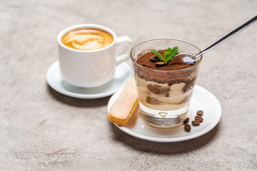 Portion of Classic tiramisu dessert in a glass cup and espresso coffee on concrete background