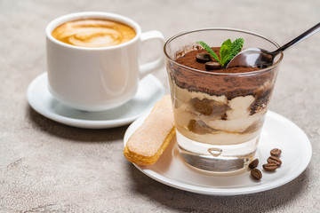 Portion of Classic tiramisu dessert in a glass cup and espresso coffee on concrete background