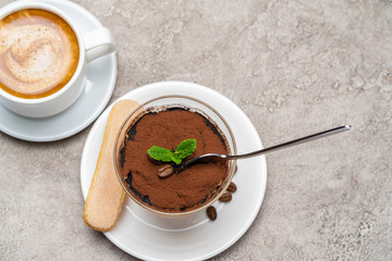 Portion of Classic tiramisu dessert in a glass cup and espresso coffee on concrete background