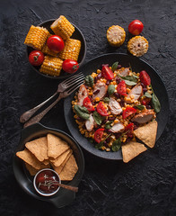 Mexican vegetable and chicken salad with nachos on black dark background. Corn, tomatoes, peppers, beans. Taco mix. The view from the top.