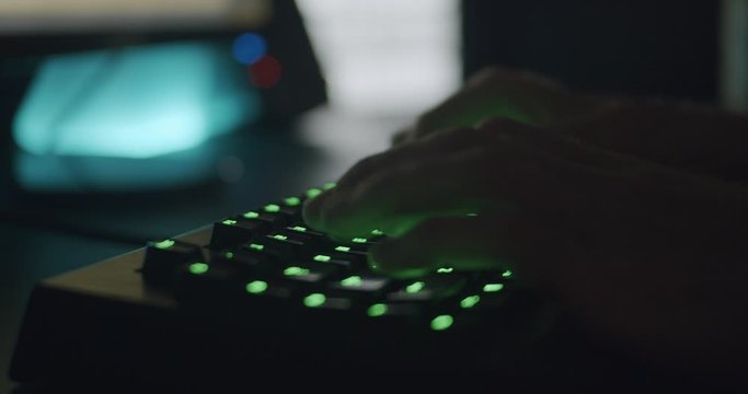 Hands Typing on Gaming Keyboard Glowing Green in Dark Room 