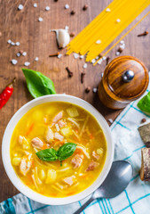 Chicken soup with noodles and vegetables in white bowl on wooden table background
