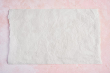 Crumpled piece of white parchment or baking paper on rose and white texture pattern background. Top view. Copy space for text and design element.