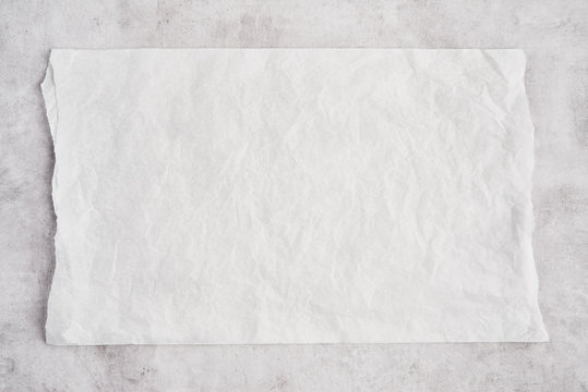 Crumpled piece of white parchment or baking paper on grey concrete background. Top view. Copy space for text and design element.