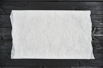 Crumpled piece of white parchment or baking paper on black wooden table. Top view. Copy space for...