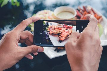 Camera eats first concept: man taking pictures food on the table with smartphone for social media sharing or check in before eating launch food