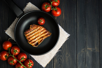 appetizing grilled pork steak and tomato in a pan on a dark wooden background