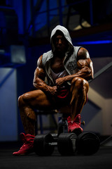 Fototapeta na wymiar Bodybuilder in Hooded Jacket Sitting on a Bench at the Gym