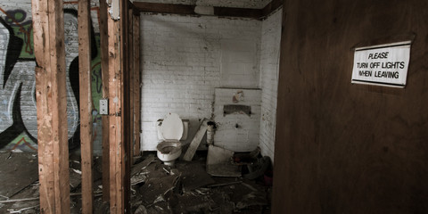 Decaying bathroom with an open door depicting an ironic sign reading “Please turn off lights when leaving” inside an abandoned, dilapidated Detroit factory
