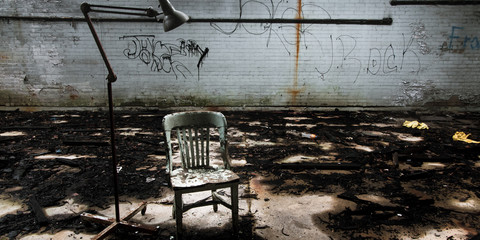 Chair and floor lamp in a ruined Detroit factory interior, conveying the feeling of an...