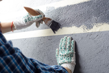 female painting a wall with masking tape and brush