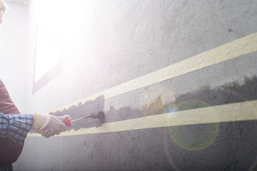 female painting a wall with masking tape and roller