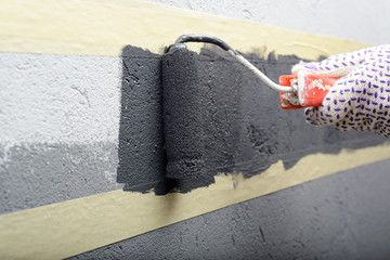 female painting a wall with masking tape and roller