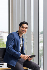 Young Asian businessman smiles and enjoys the job in a comfortable holding the tablet in the office