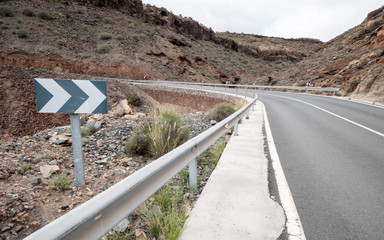 Warning sign and bend in road. An empty road curving into the rocky hillside in a hot and arid...