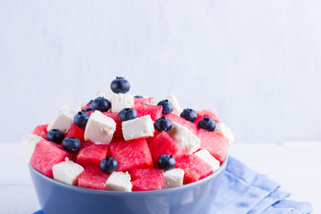 Watermelon salad with feta cheese on blue napkin. Healthy salad with blueberries, watermelon and soft cheese. Summer salad with a fork on white background