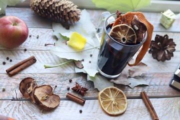 Cup with mulled wine, autumn leaves, seasonal fruits and vegetables, decor, spices on a window background, home comfort concept