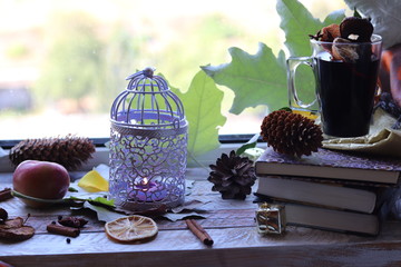 Cup with mulled wine, autumn leaves, seasonal fruits and vegetables, decor, spices on a window background, home comfort concept