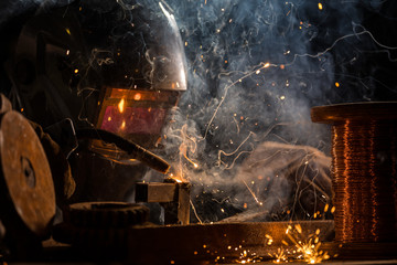 Welder is welding metal part in industrial workshop.