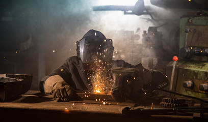 Welder is welding metal part in industrial workshop.