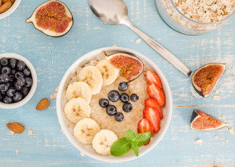 oatmeal with blueberries, strawberries, figs, banana and almonds. Healthy breakfast on a wooden blue background. Top wiev
