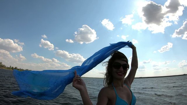 Slender girl with a big scarf on the shore. A woman holds in wind a developing scarf pareo stands near the river.