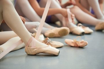 Tying ballet slippers close up. Young ballerina sitting on the floor and tying her ballet shoes. How to put on ballet footwear. © DenisProduction.com