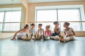 Fototapeta premium Group of ballerinas talking to each other in studio. Beautiful young ballet dancers having break in practice. Friendship in ballerinas team. Big dreams of little girls.