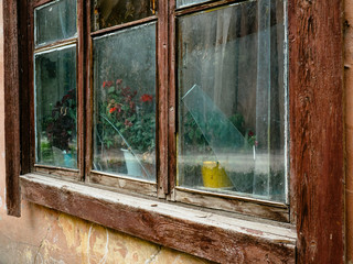 Old broken window with flowers. Dirty glass of an old house