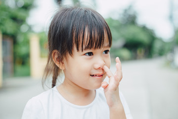 Portrait of little Asian girl pick the nose that is not good behavior in public place.