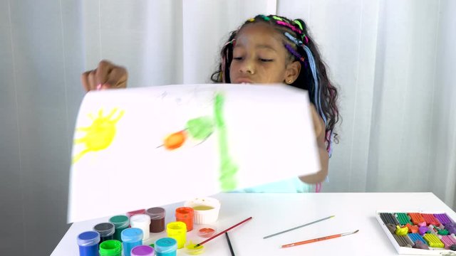 Mixed ethnicity girl with colored braids has finished coloring the image with acrylic paint. Creative activity at home