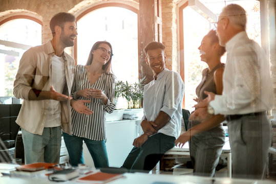 Happy at work. Group of cheerful people smiling and discussing something while standing in the modern office
