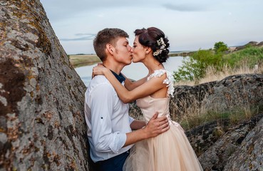 Loving couple, guy and girl kiss and hug on stones against the background of the river. Wedding day.